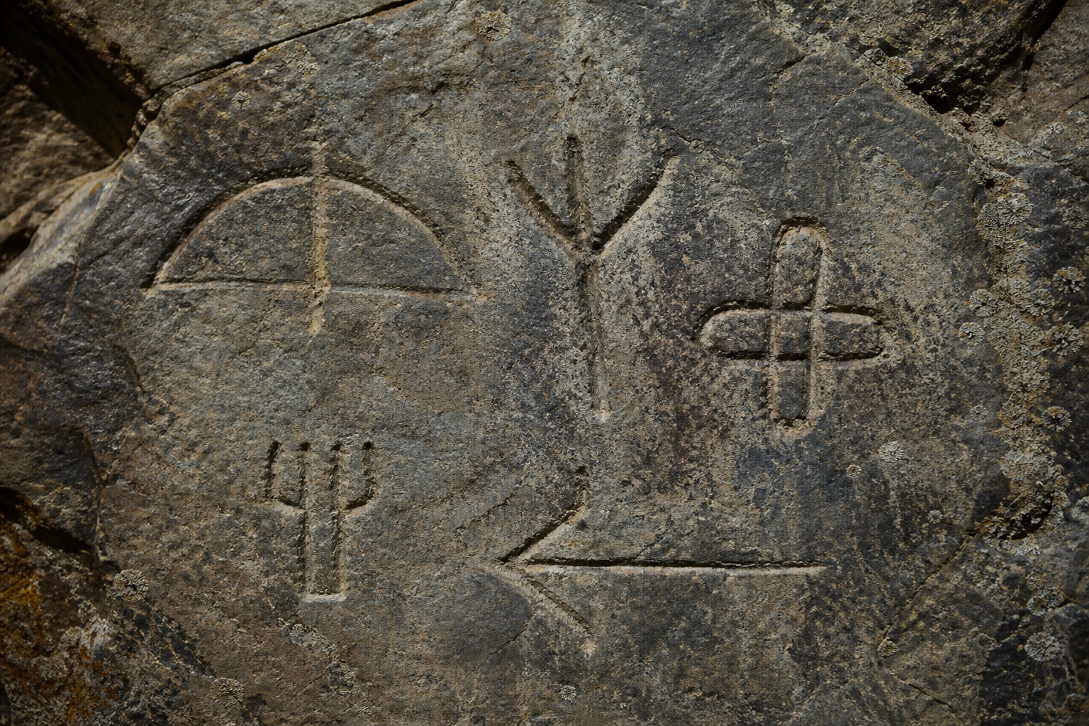 Weathered Central Asian rock face with incised geometric clan marks, the kind of tamga signs used to record presence and lineage